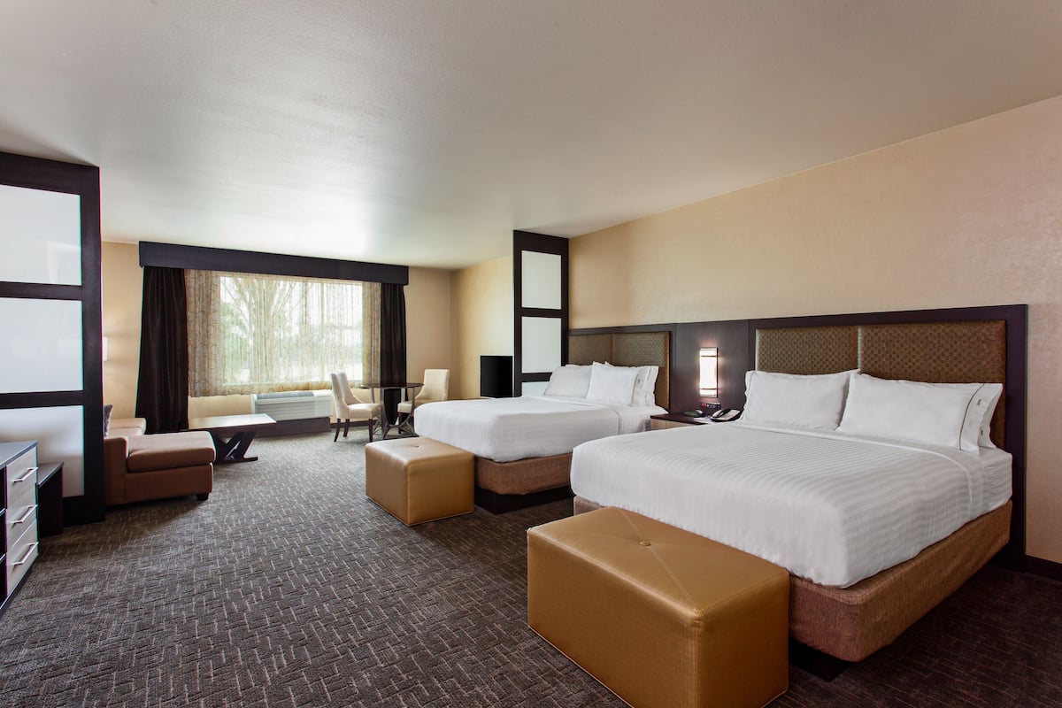 A hotel room with two beds, a desk, a chair, and a large window.