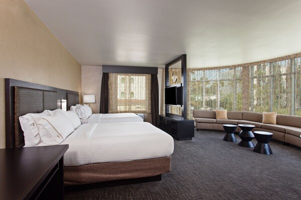 A hotel room with a large bed, a sofa, a TV, and a view of trees through the windows. - Holiday Inn Express & Suites Anaheim Resort Area by IHG (Anaheim)