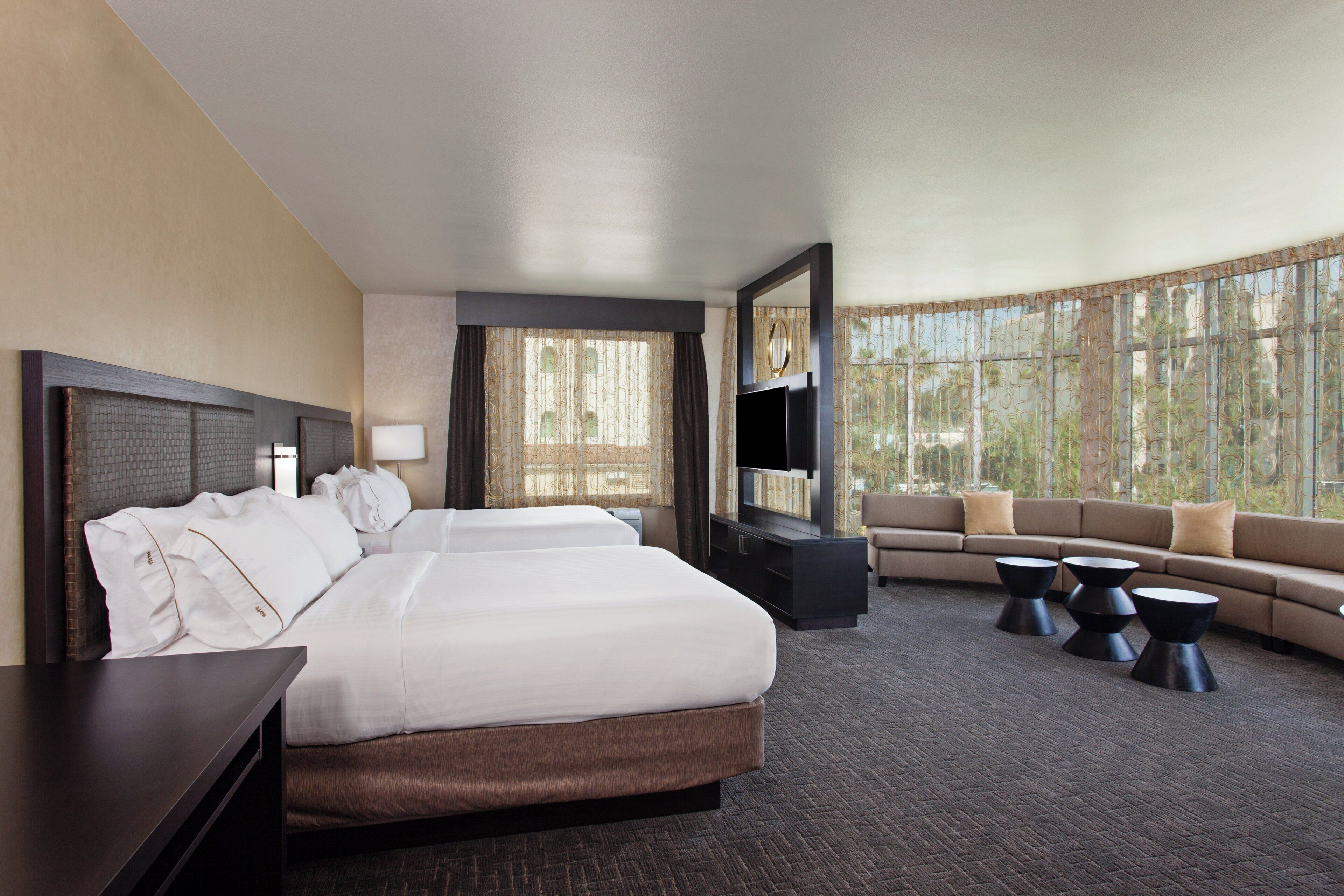A hotel room with a large bed, a sofa, a TV, and a view of the outdoors.