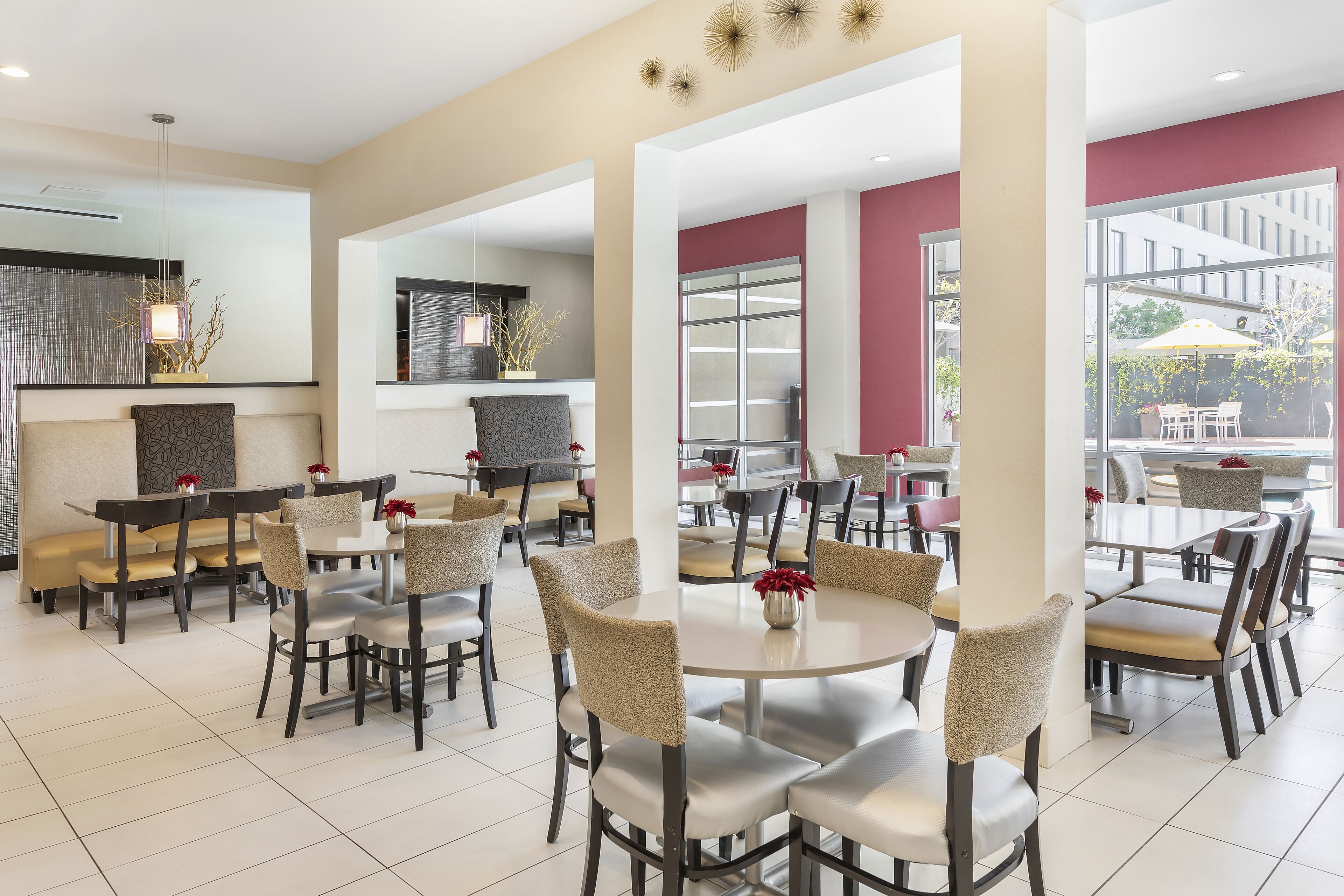 Un'area pranzo moderna con tavoli e sedie rotonde, una grande finestra con vista sull'esterno e un lampadario decorativo.