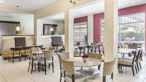 A modern dining area with round tables and chairs, a large window with a view of the outdoors, and a decorative ceiling light fixture. - Holiday Inn Express & Suites Anaheim Resort Area by IHG (Anaheim)