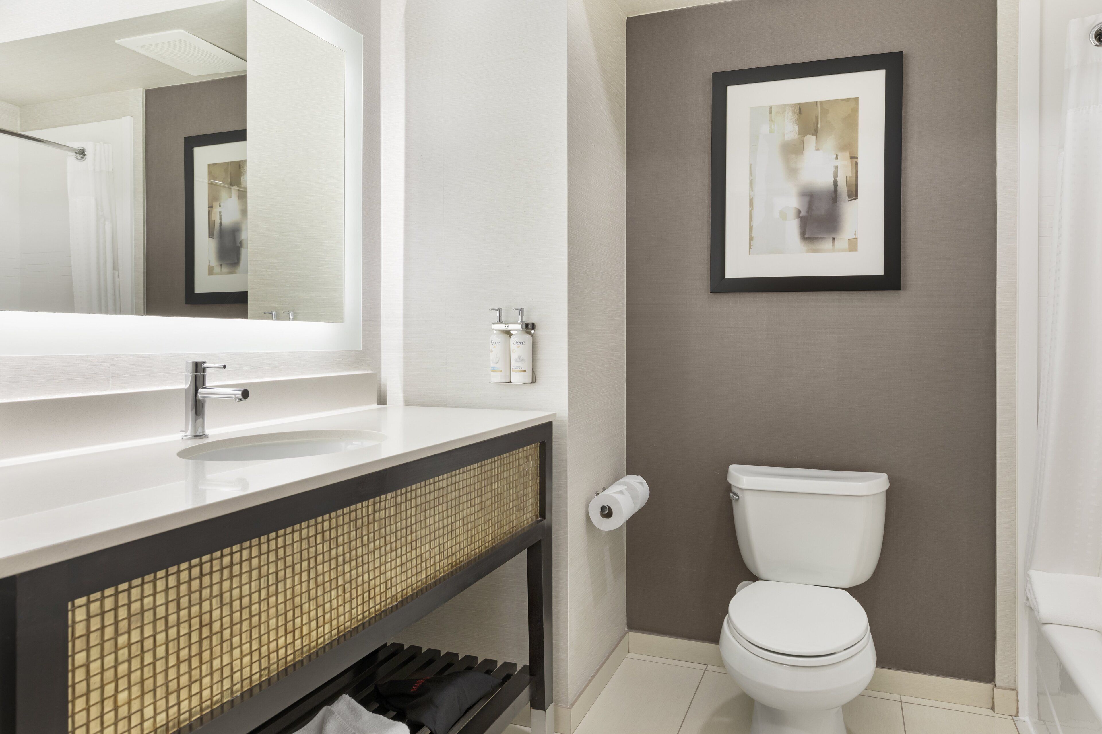 A modern bathroom with a large mirror, a sink, a toilet, and a framed picture on the wall.