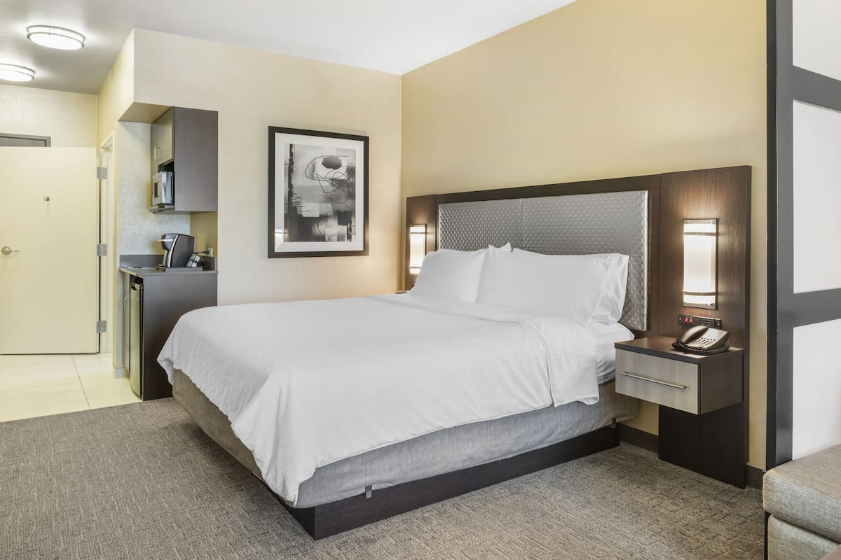 A hotel room with a large bed, a bedside table with a phone, a small desk with a lamp, and a framed picture on the wall.