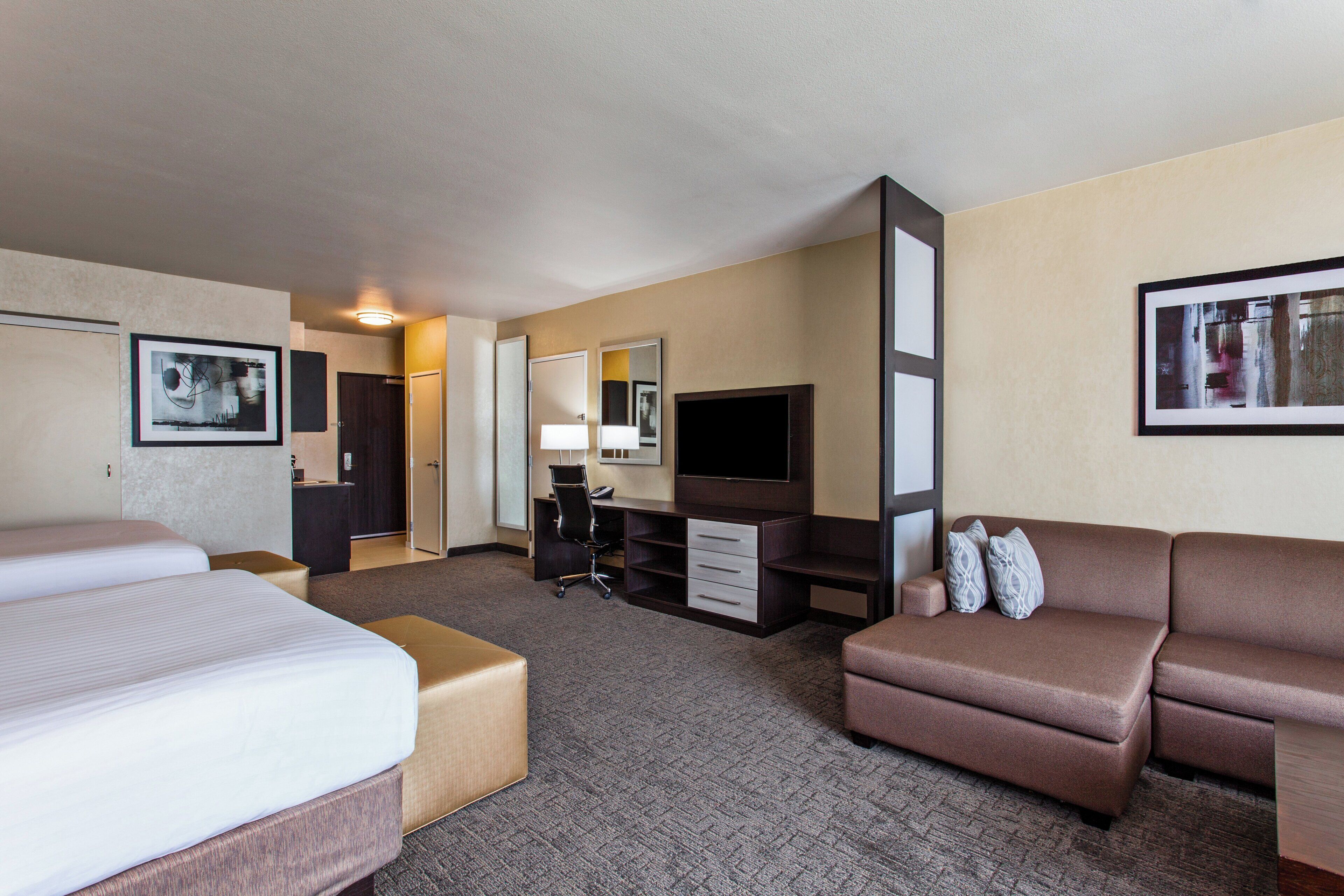A hotel room with two beds, a desk, a television, and a sofa.