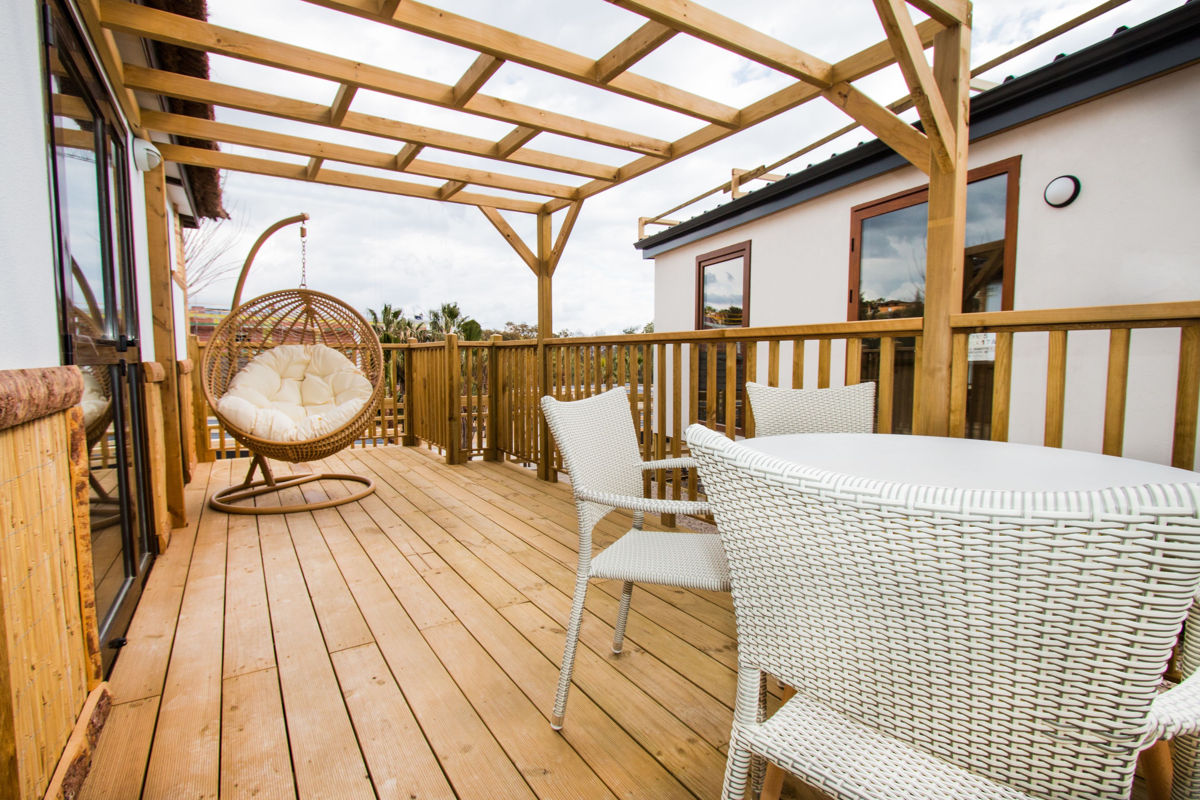 Una terraza de madera con mobiliario de mimbre, incluyendo una silla colgante y una mesa con sillas.
