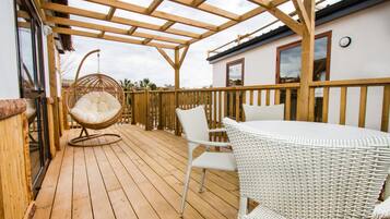 Una terraza de madera con mobiliario de mimbre, incluyendo una silla colgante y una mesa con sillas.