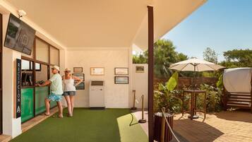 A reception area with a green artificial turf floor, a reception desk, and a wooden fence enclosing a patio area with outdoor seating and umbrellas.