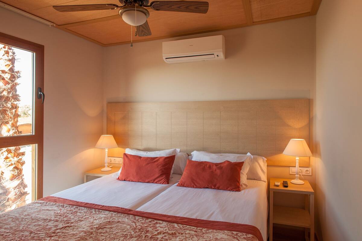 Ein Hotelzimmer mit zwei Betten, einem Deckenventilator, einer Klimaanlage, einem Nachttisch mit Lampe, einem Badezimmer mit Waschbecken und Toilette sowie einer Dusche.