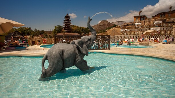 A pool area with a large elephant statue, a pagoda-style building, and a clear blue sky. - Magic Natura Animal, Waterpark & Polynesian Resort (Benidorm)