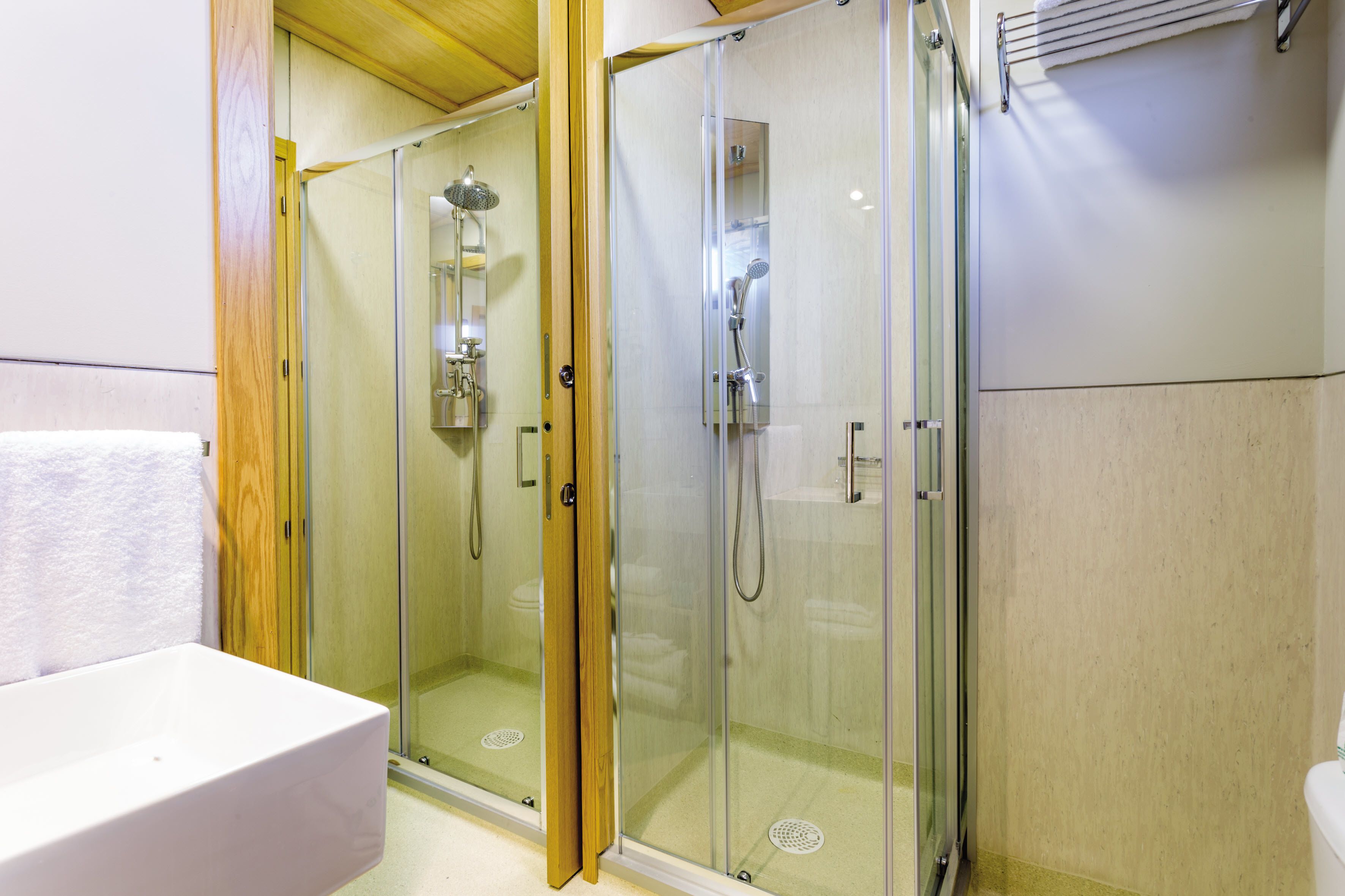 Un área de ducha con paredes de vidrio, un lavabo blanco y una puerta de madera.