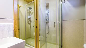 Un área de ducha con paredes de vidrio, un lavabo blanco y una puerta de madera.