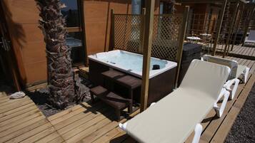 Terraza de madera con jacuzzi, sillas de descanso y una palmera.