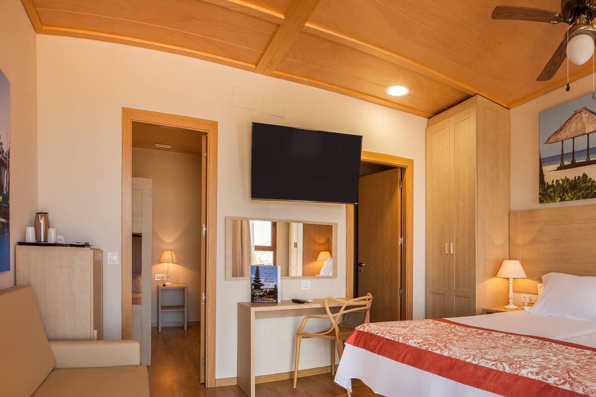 Ein Hotelzimmer mit Bett, Schreibtisch, Stuhl und einem Gemälde einer Strandansicht.