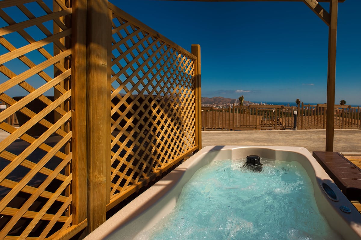 Ein Whirlpool mit Holzjalousien im Hintergrund, freie Sicht auf die Landschaft und ein Poolbereich.