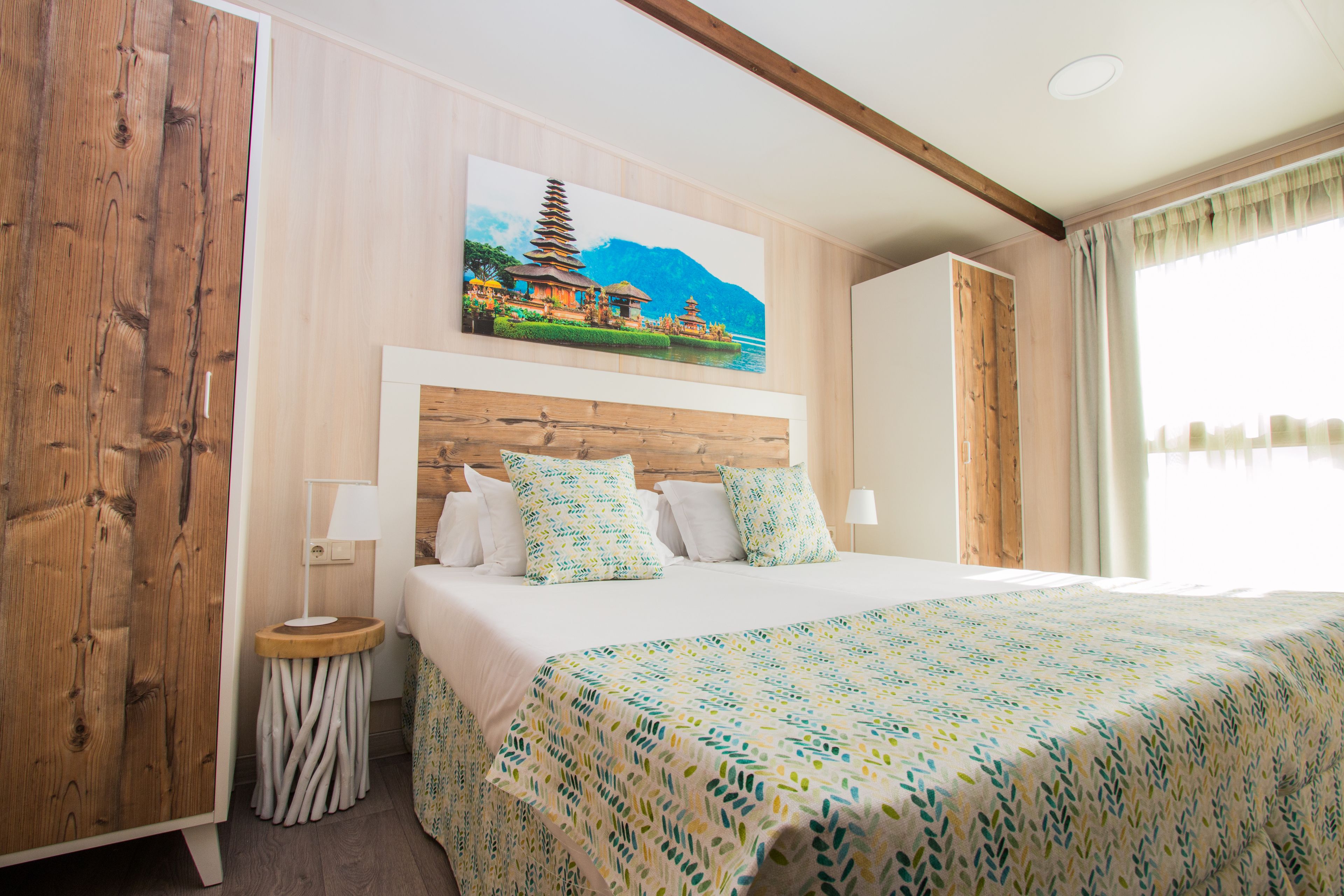 A hotel room with a large bed, a wooden headboard, a nightstand, a lamp, and a painting of a pagoda on the wall.