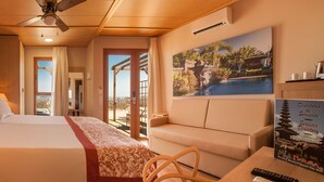 A hotel room with a bed, a sofa, a ceiling fan, a painting of a tropical scene, and a remote control on the table. - Magic Natura Animal, Waterpark & Polynesian Resort (Benidorm)