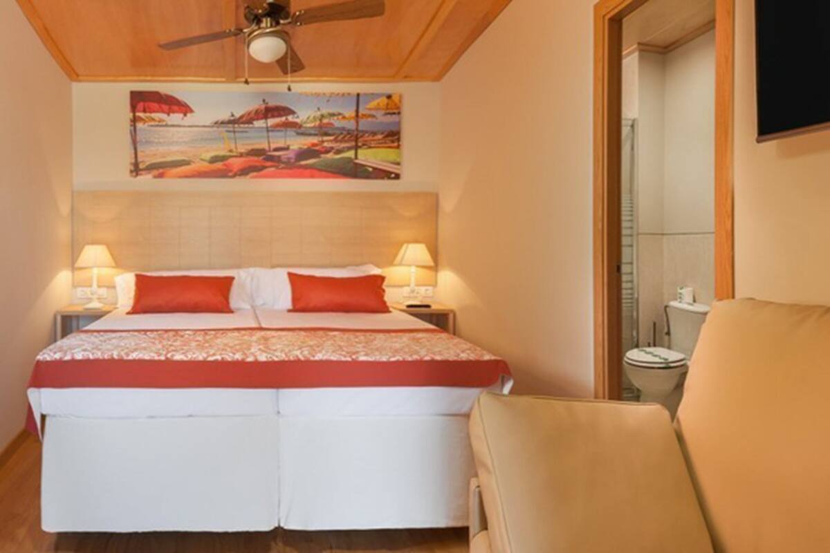 Ein Hotelzimmer mit einem Bett, zwei Nachttischlampen, einem Deckenventilator und einem Gemälde über dem Bett.