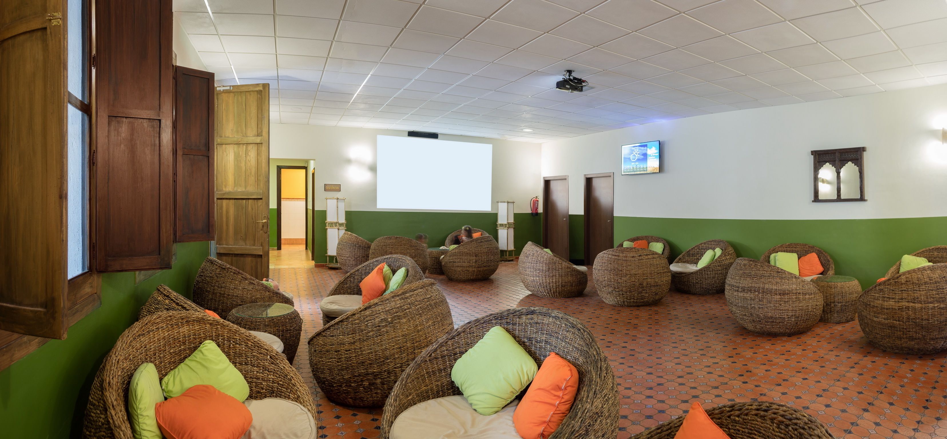 A room with wicker chairs, a projector screen, and a green and white wall.