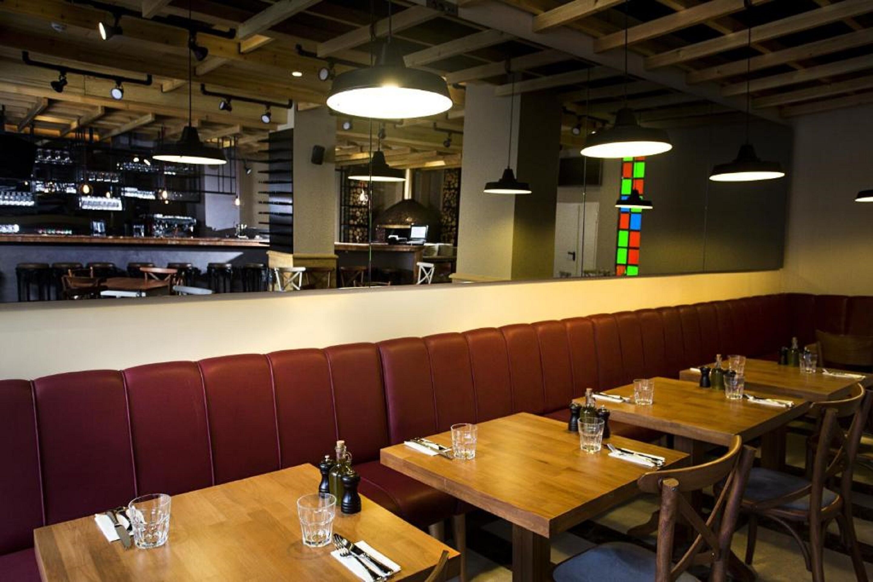 Un interior de restaurante con mesas de madera, asientos tapizados en rojo y lámparas colgantes.