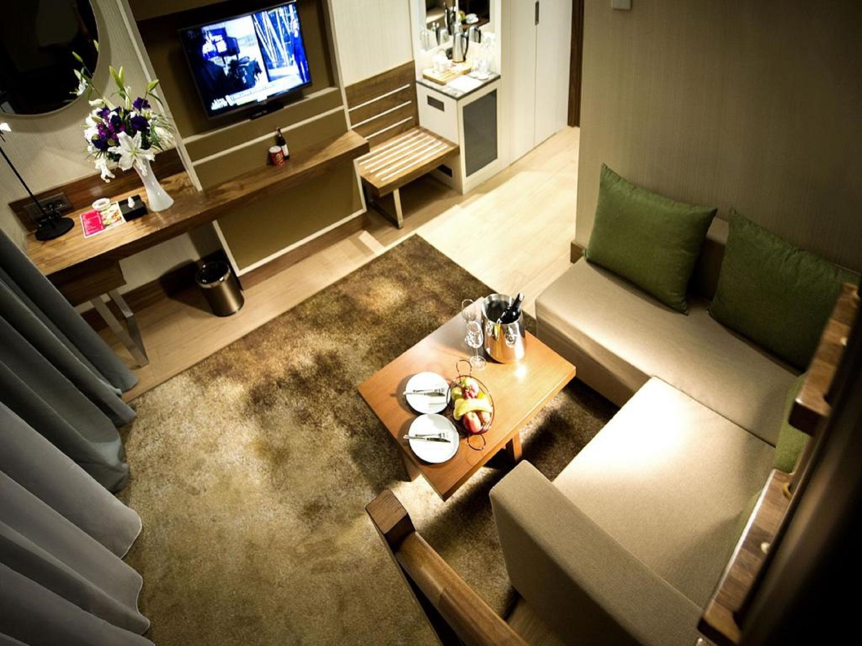 Una sala de estar moderna con un banco de madera, una mesa de centro con frutas y vasos, un televisor y un sofá con cojines verdes.