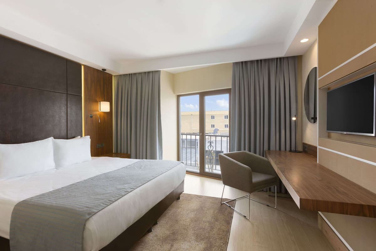 A hotel room with a large bed, a desk, a TV, and a balcony with curtains.
