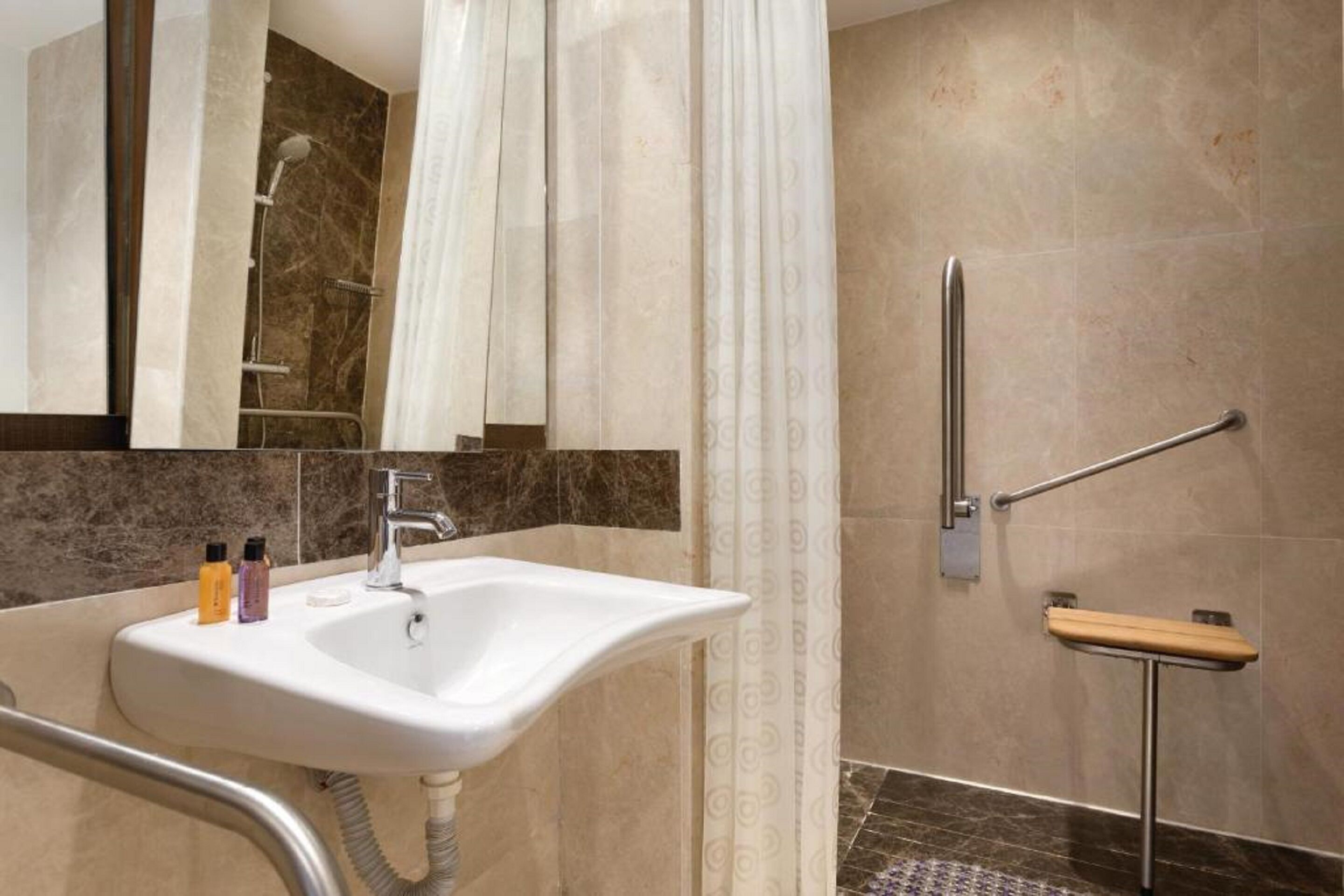 A bathroom with a sink, mirror, shower, and grab bar.