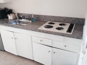 A kitchen with white cabinets, a granite countertop, a stainless steel sink, and a four-burner stove.