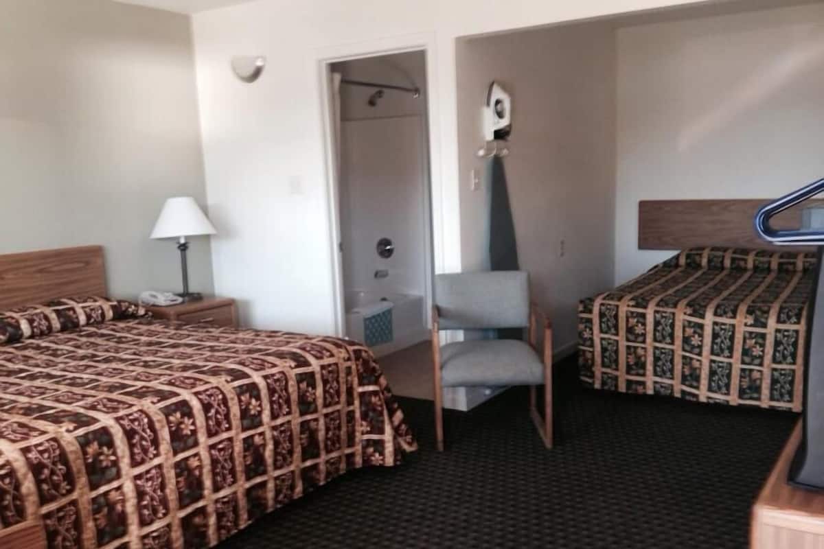 A hotel room with two beds, a chair, a desk, a lamp, and a mirror.