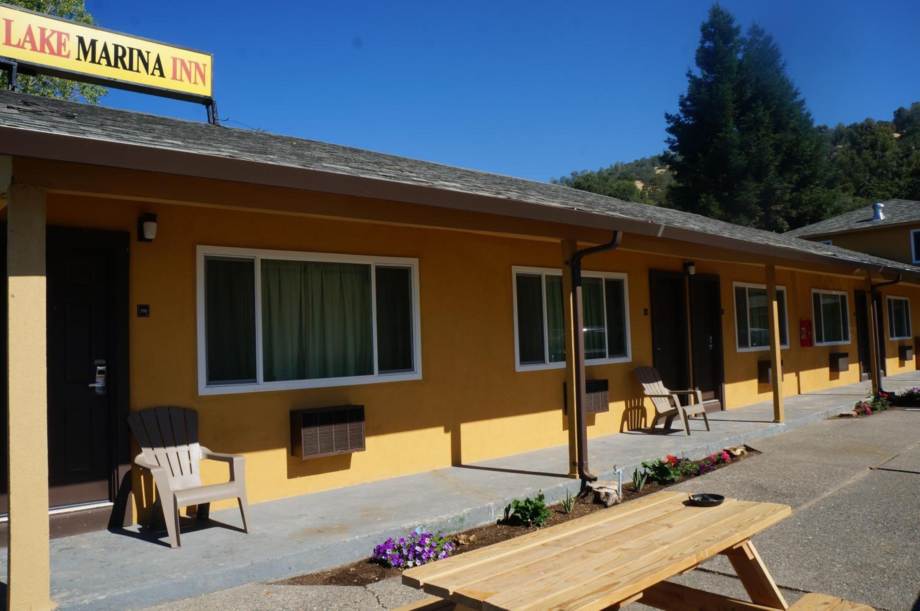 Filera de habitacions d'un motel grogues amb finestres grans, seients a l'exterior i un rètol que diu "LAKE MARINA INN".