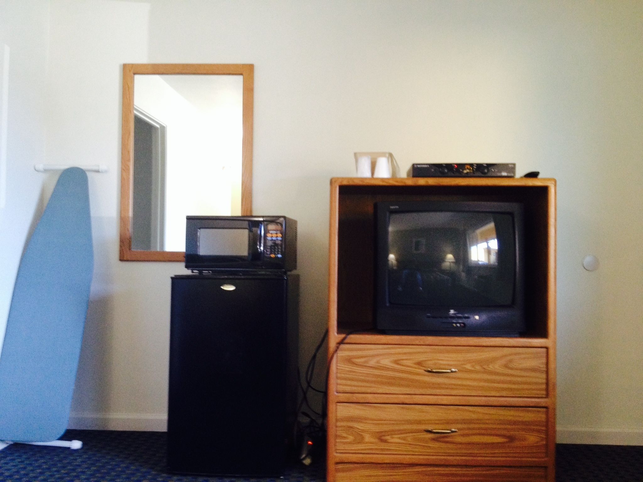 Una habitación compacta con un mueble bajo de televisión de madera, un microondas y una tabla de planchar azul.