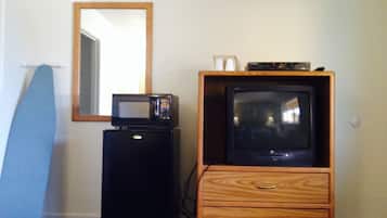 Una habitación compacta con un mueble bajo de televisión de madera, un microondas y una tabla de planchar azul.
