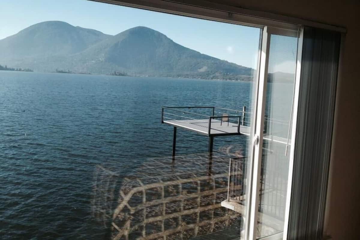 A view from a window overlooking a calm lake with mountains in the background.