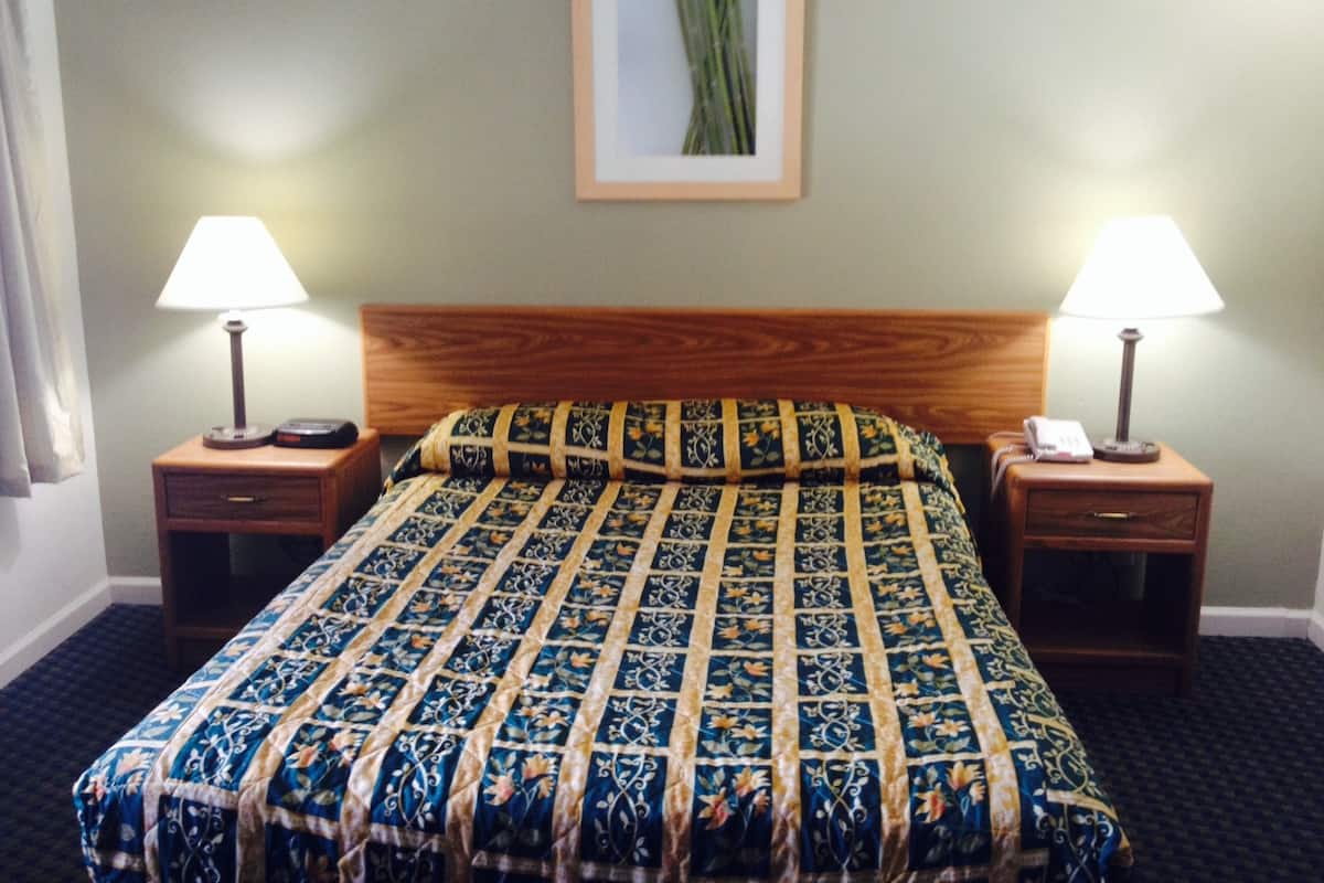 A hotel room with a wooden headboard, a floral-patterned bedspread, two bedside tables with lamps, and a framed picture on the wall.
