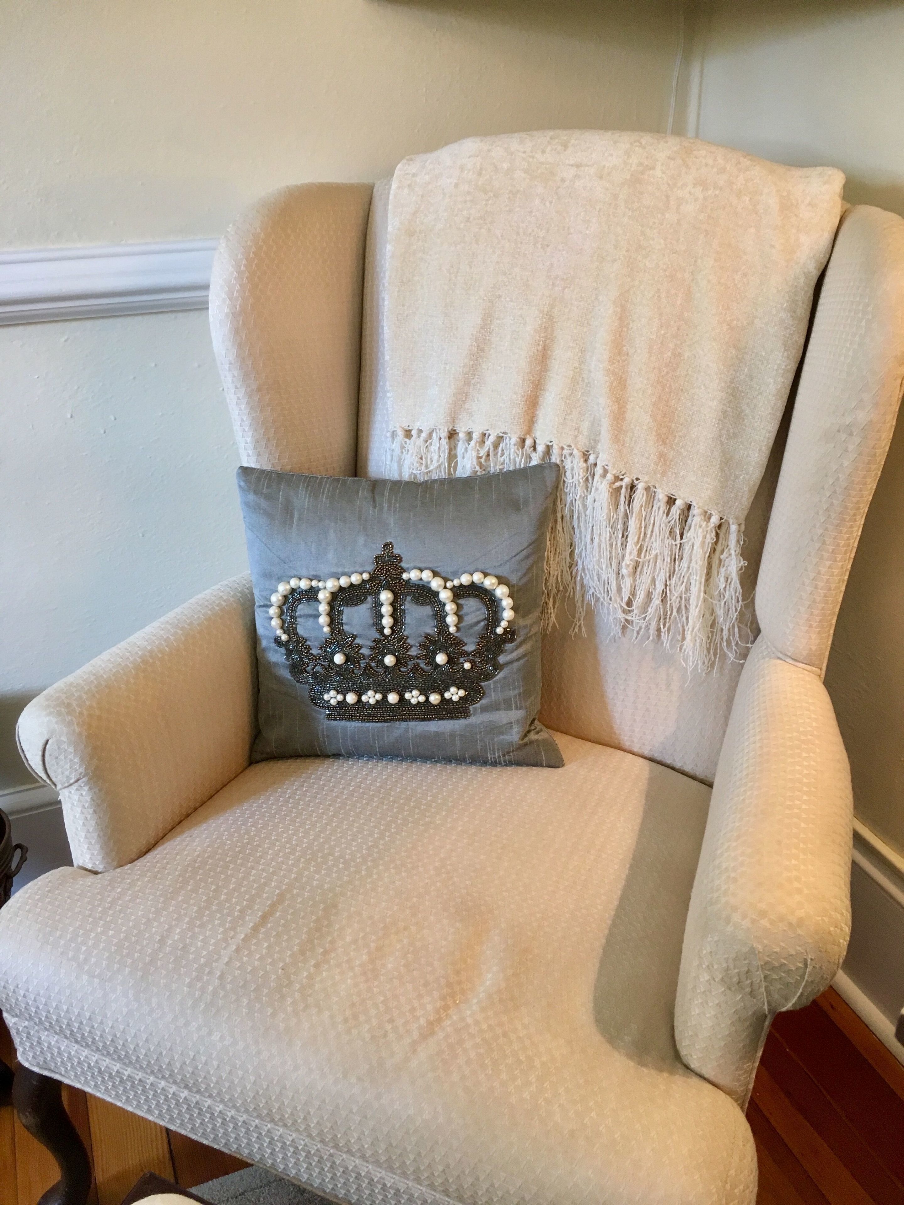 A beige armchair with a gray cushion featuring a crown design.
