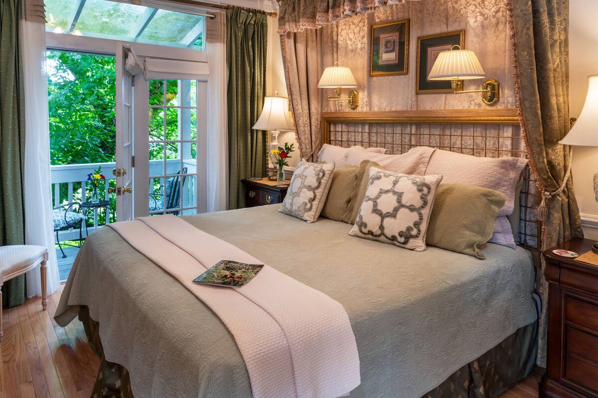 Une chambre à coucher avec un grand lit, deux tables de chevet, une fenêtre avec des rideaux et une vue sur la verdure à l’extérieur.
