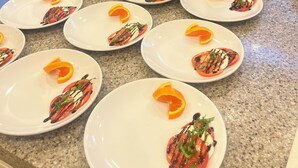 A kitchen counter with plates of food, a person pouring a sauce, and kitchen cabinets in the background.