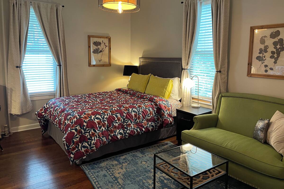 A bedroom with a bed, a green sofa, a glass coffee table, and a hanging light fixture.