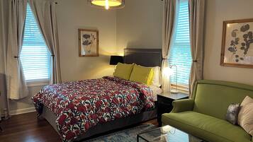 A bedroom with a bed, a green sofa, a glass coffee table, and a hanging light fixture.