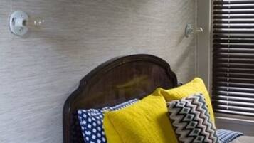 A bedroom with a wooden headboard, a bed with patterned bedding, a nightstand with a green object, and a window with blinds.