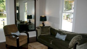A living room with a brown armchair, a wooden coffee table, a green sofa, and a lamp on a side table. - Modern Homestead Guest House (Reedsville)
