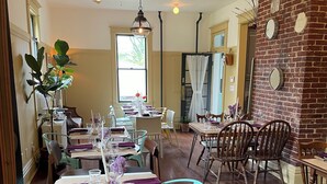 A dining area with wooden tables and chairs, a brick wall, and hanging light fixtures. - Modern Homestead Guest House (Reedsville)