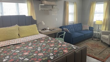 Een compacte hotelkamer met een bed, een blauwe bank, een klein bureau en een stoel.