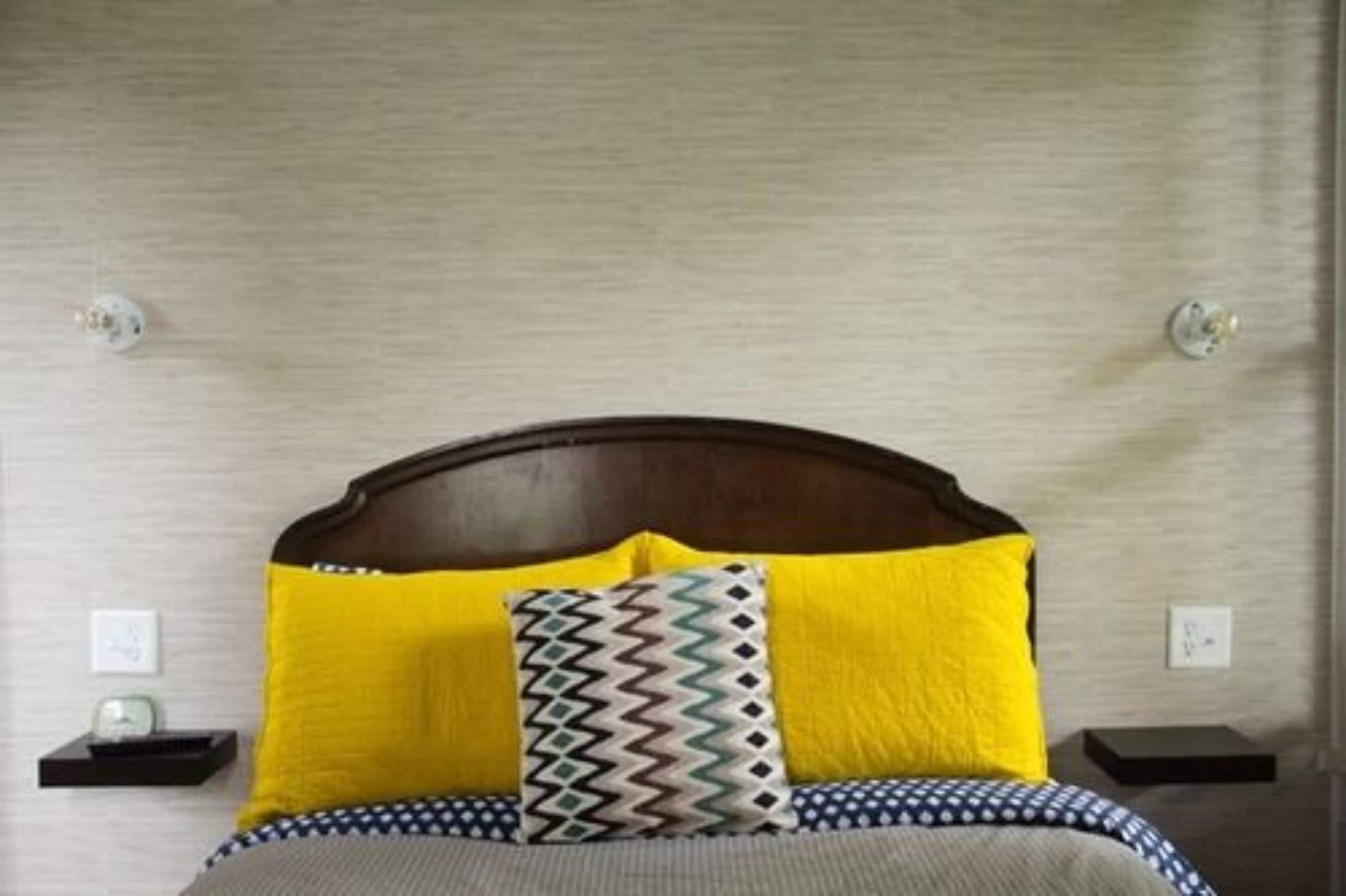 A bed with a wooden headboard, two yellow pillows, and a patterned pillow.