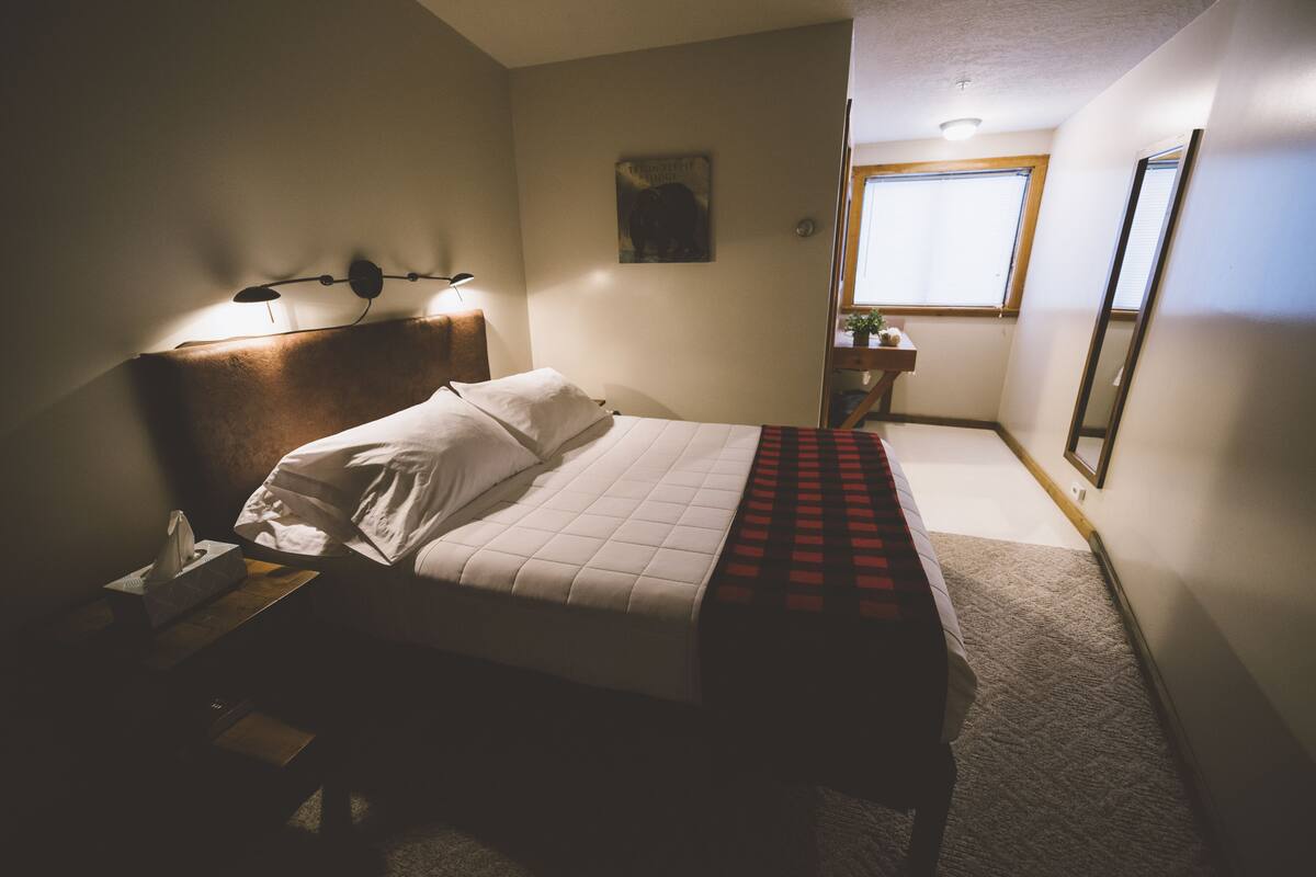 A bedroom with a bed, bedside table, lamp, and a window.