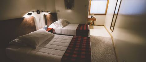 A hotel room with two beds, a nightstand, a lamp, a painting on the wall, and a window.