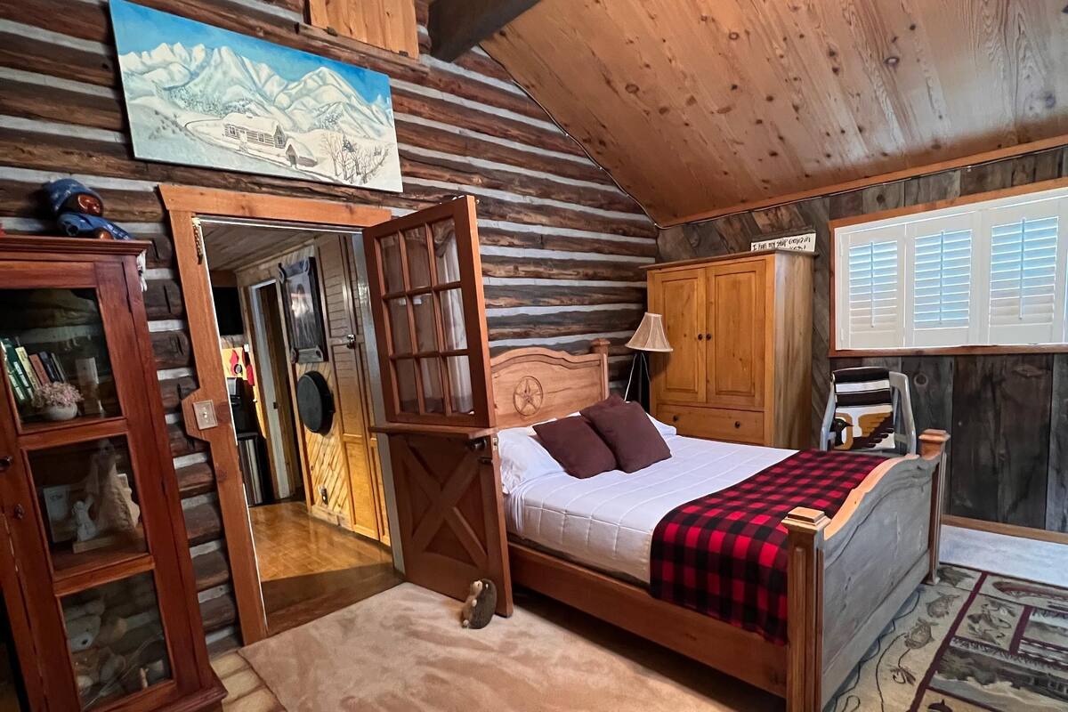 A cozy log cabin bedroom with a wooden four-poster bed, a wooden wardrobe, and a painting of a mountain landscape.
