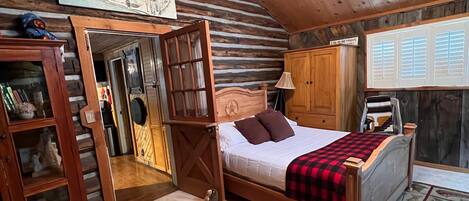 A cozy log cabin bedroom with a wooden four-poster bed, a wooden wardrobe, and a painting of a mountain landscape.
