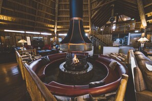 Ein gemütliches Interieur mit einem zentralen Feuerkorb, Holzmöbeln und einer hohen Decke.