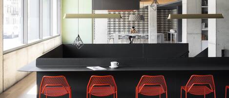 A modern bar area with a black countertop, red mesh chairs, and a view of the street through large windows.