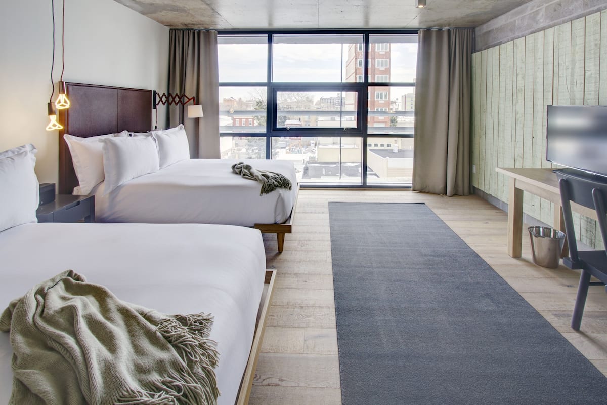 Hotellihuone, jossa on kaksi sänkyä, suuri ikkuna, työpöytä ja televisio.